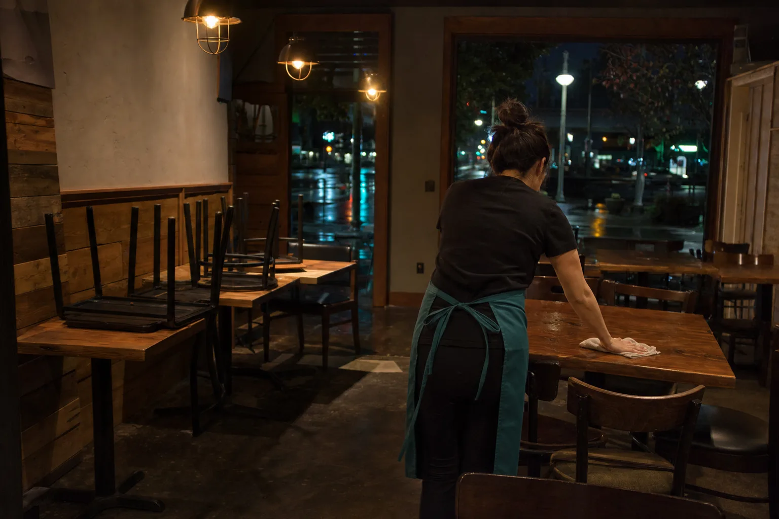 Cleaner wiping tables in an empty Gresham restaurant dining room after close